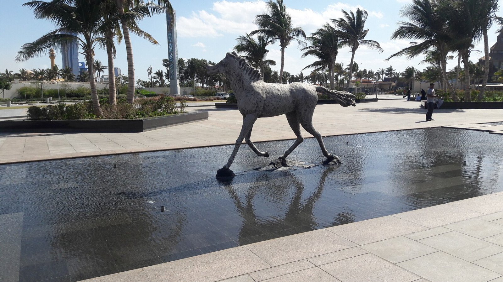 A horse sculpture above a reflecting pool among palms on the Jeddah Corniche by the Red Sea.