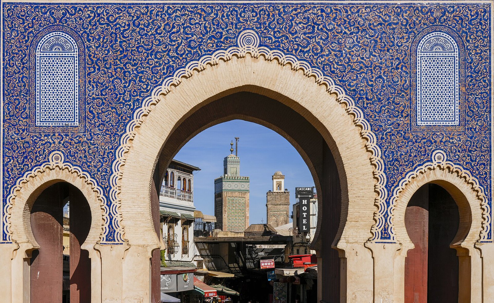 The blue-tiled horseshoe arch of Bab Bou Jeloud frames the minaret of the Bou Inania Madrasa in Fes.