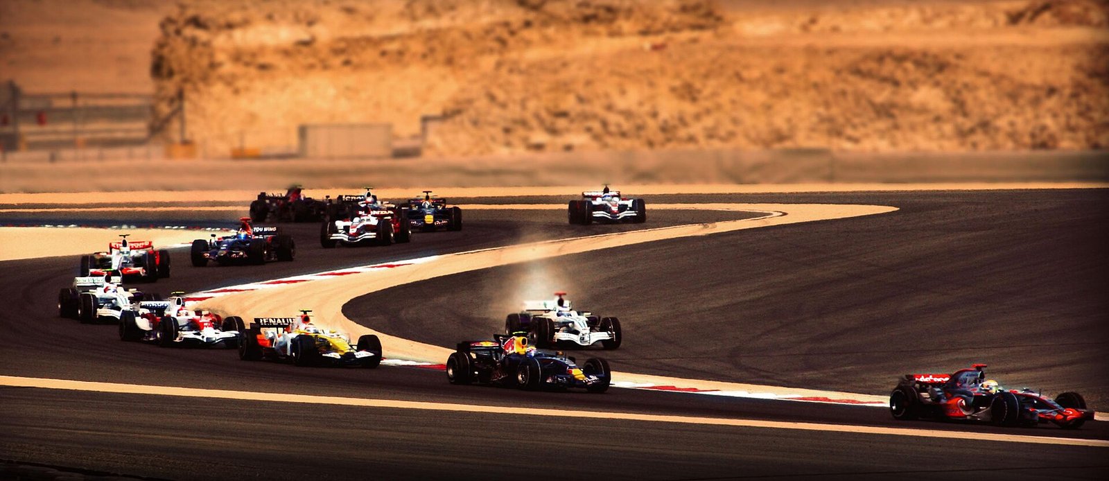Formula One cars sweeping through the first corners of the Bahrain Grand Prix at Sakhir under evening light