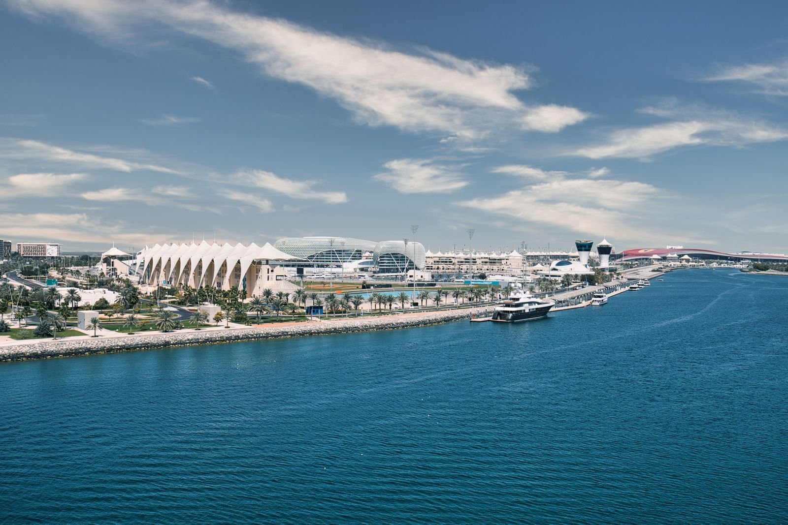 The Yas Island waterfront under a bright sky, with a yacht off Yas Marina, the W Abu Dhabi and Ferrari World's red roof on the skyline