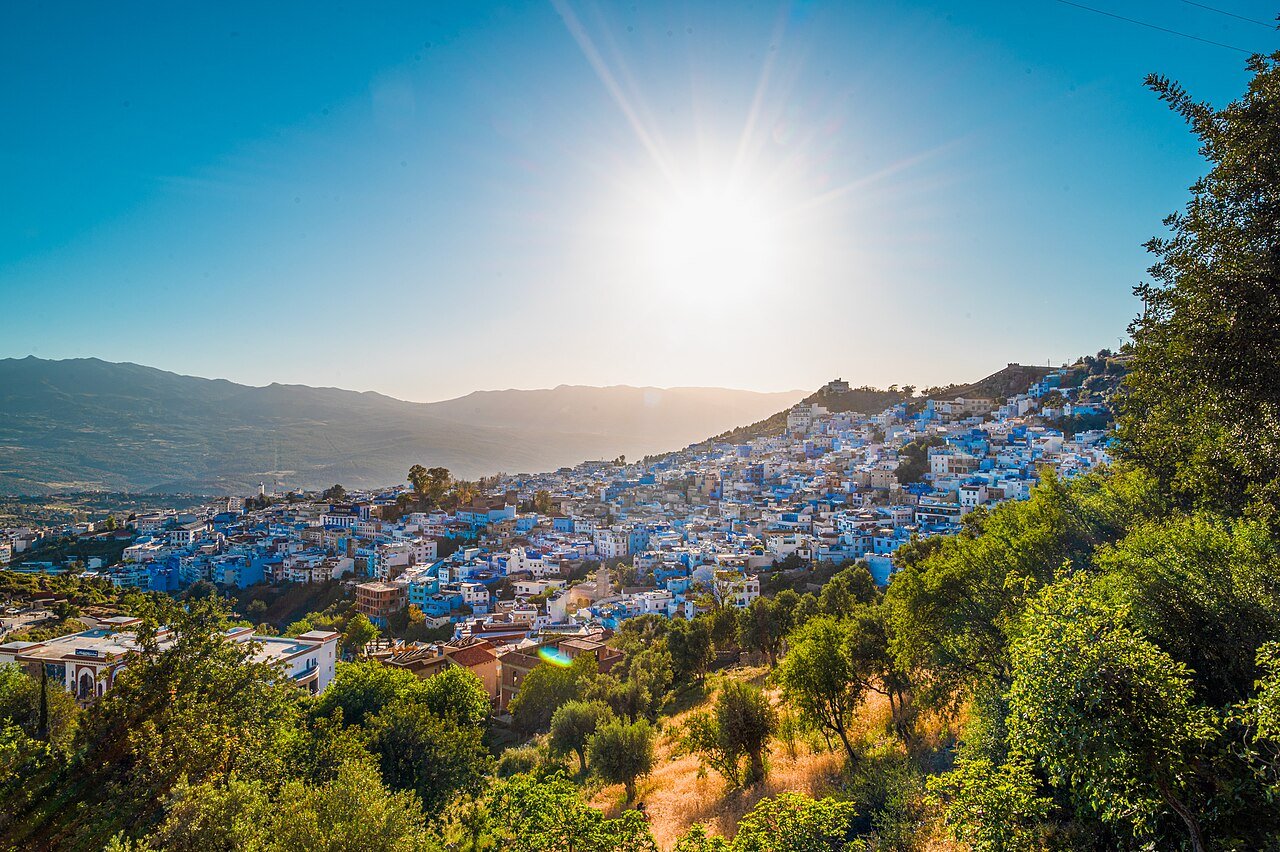 The blue-washed town of Chefchaouen spread across the green slopes of the Rif Mountains under a bright sun.
