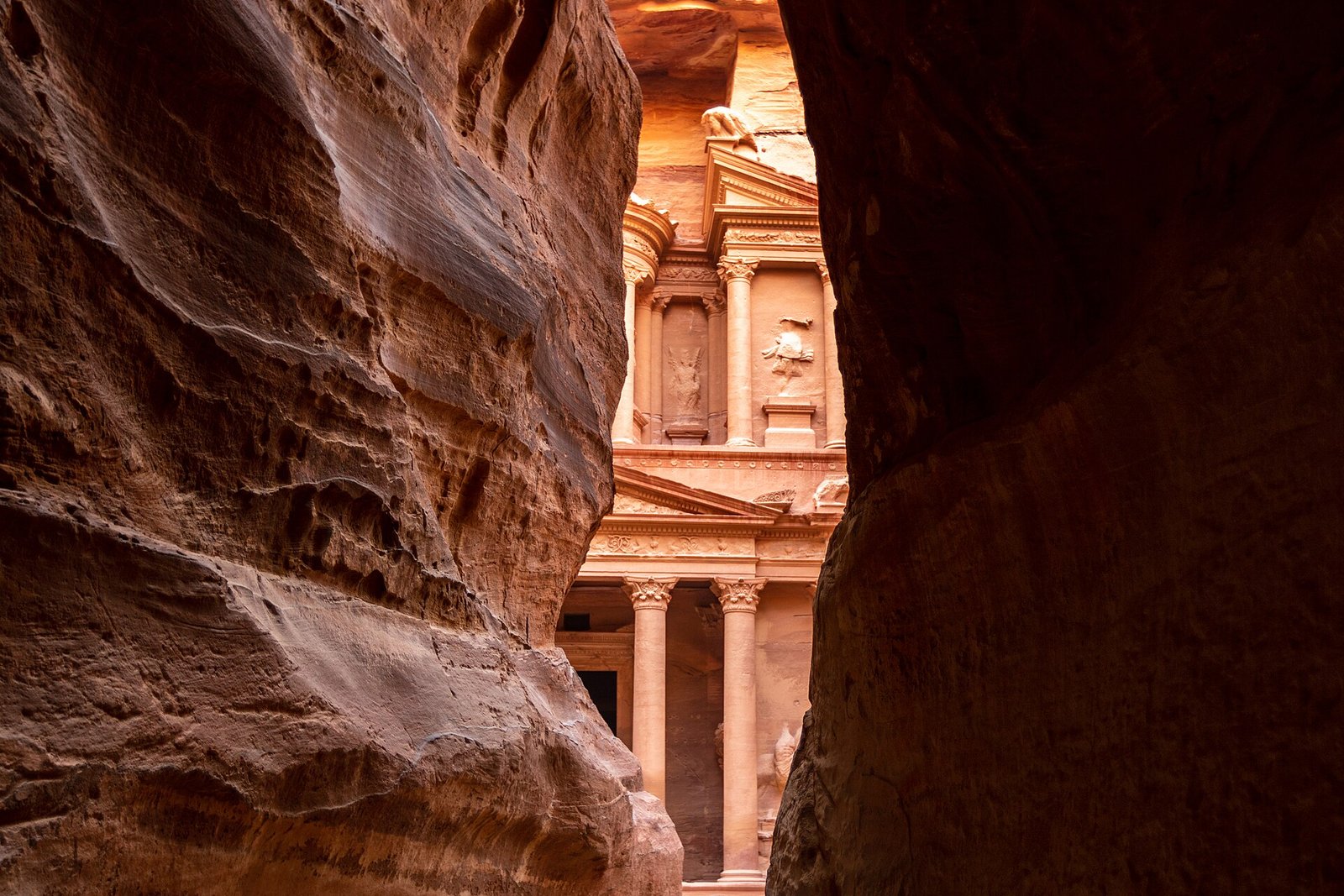 The rose-red facade of the Treasury at Petra glimpsed through the narrow walls of the Siq.