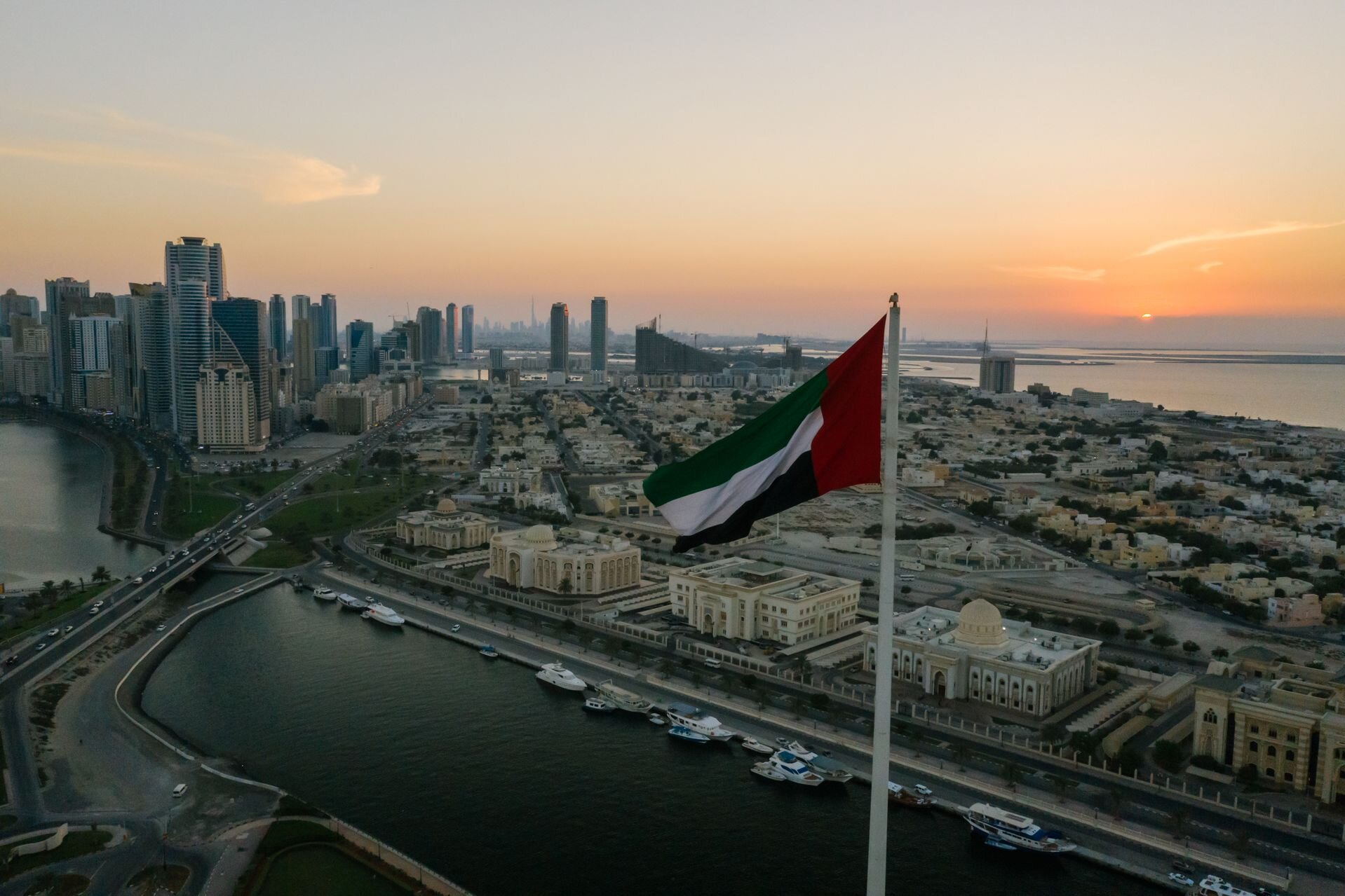 The UAE flag over Sharjah at sunset, with Khalid Lagoon and the skyline beyond