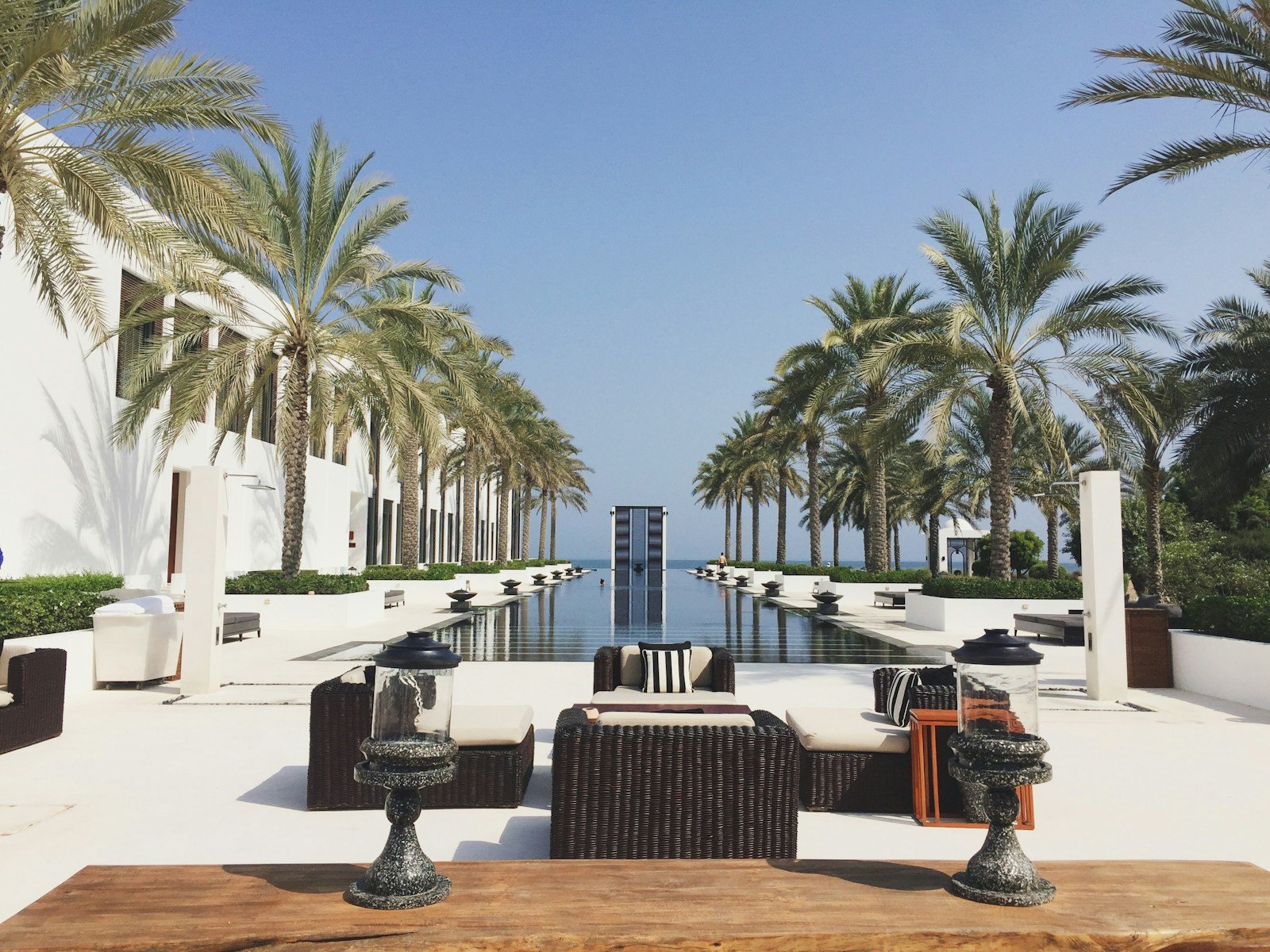 A long reflecting pool framed by date palms and white colonnades runs toward the sea at The Chedi Muscat, Oman.