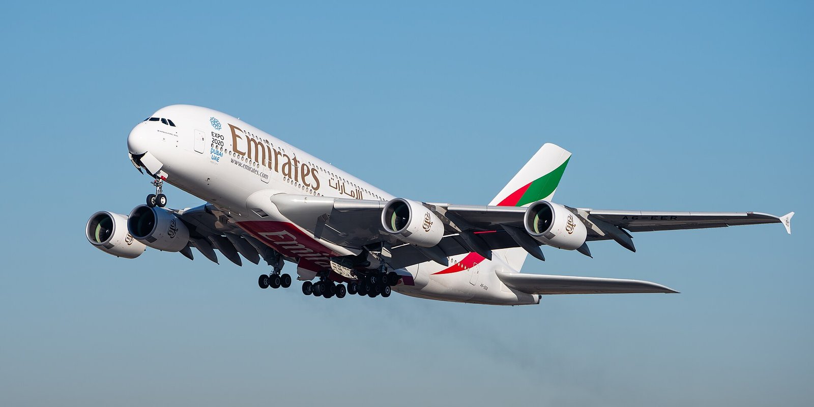 An Emirates Airbus A380 climbing after takeoff against a pale blue sky.