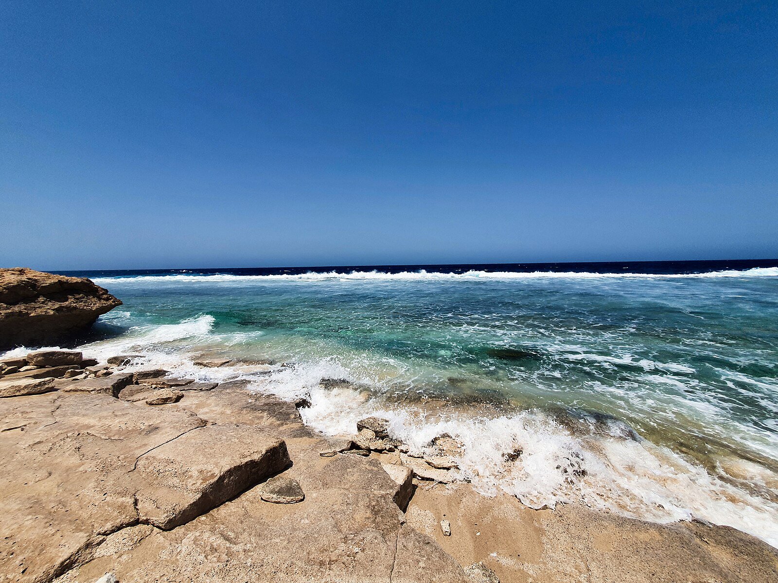 Waves breaking over a limestone shelf into turquoise water on the Red Sea coast at Umluj, gateway to The Red Sea resorts.