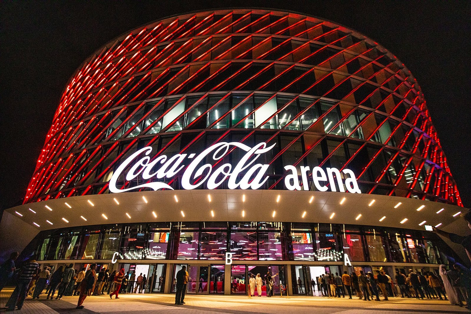 The red-lit lattice facade of Coca-Cola Arena glows above its entrance at night in Dubai.