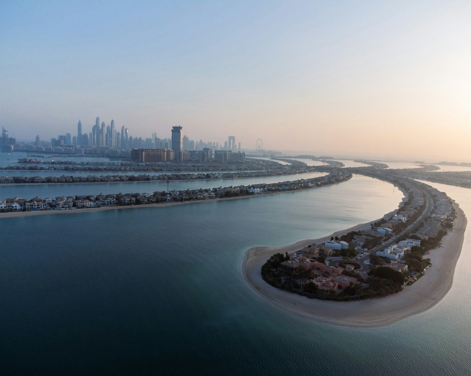 Beachfront villas line the curving fronds of the Palm Jumeirah at dawn, with the towers of Dubai Marina on the horizon