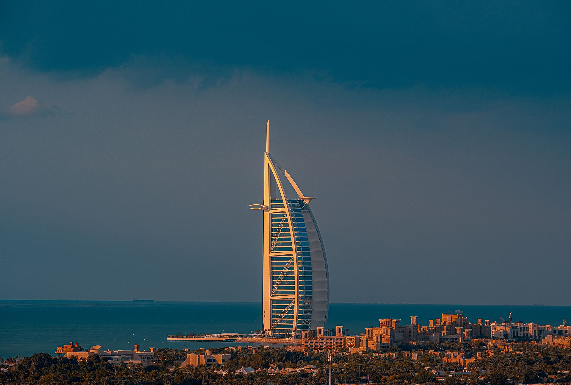 The sail-shaped Burj Al Arab lit gold by the evening sun against a dark sky, above Madinat Jumeirah and the sea