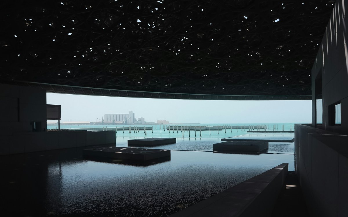 Light falls through the latticed dome of the Louvre Abu Dhabi onto still water opening to the Arabian Gulf.