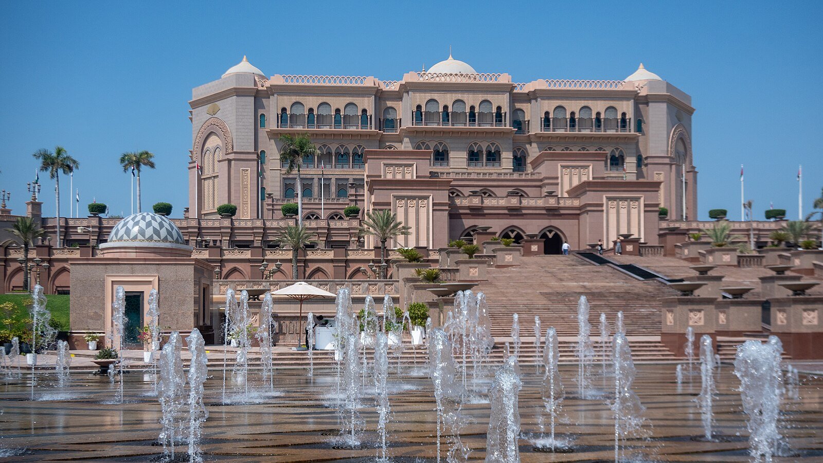 Dancing fountains on the forecourt of Emirates Palace, its rose-toned facade and domes set against a clear Abu Dhabi sky