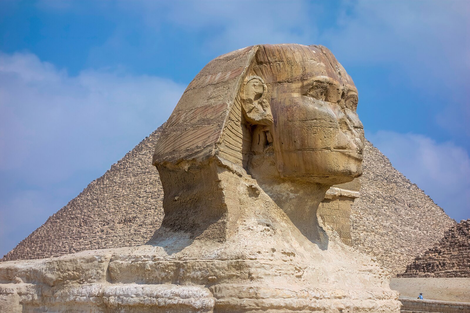 The head of the Great Sphinx in profile against the Great Pyramid of Giza and a soft blue sky