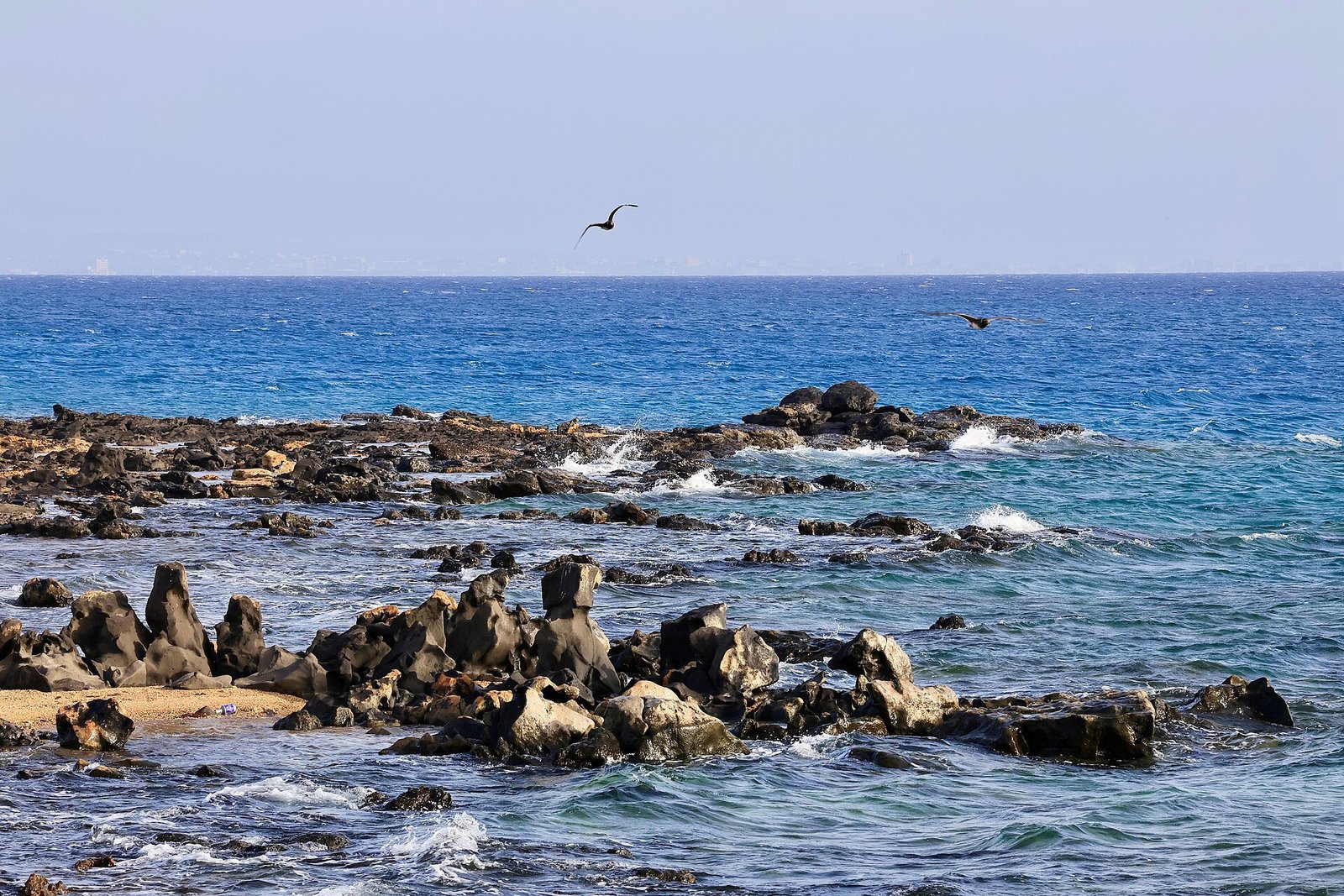 Clear blue Red Sea water breaking over dark volcanic rocks at Harrat beach, Umluj, on Saudi Arabia's northwest coast.