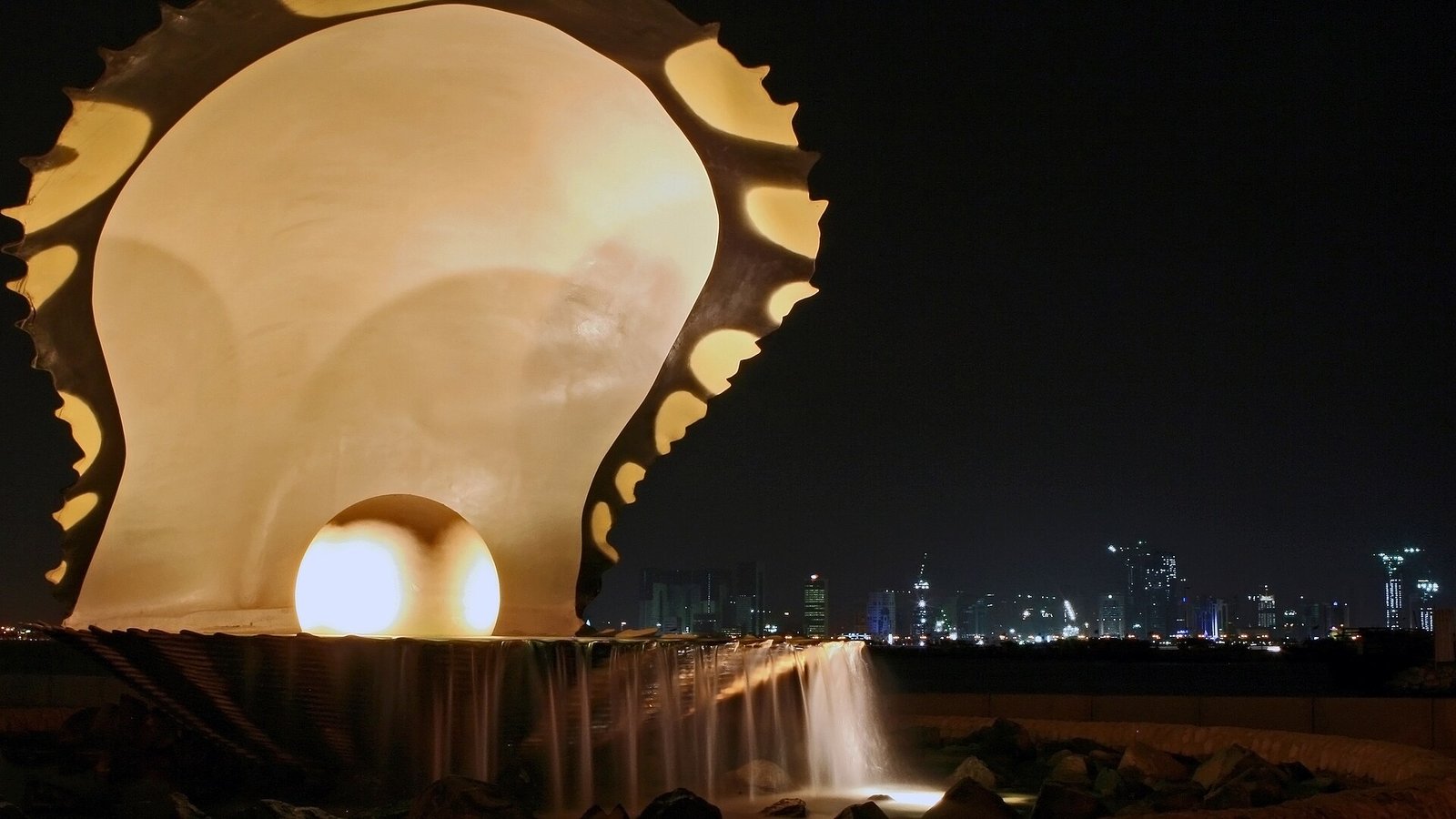 The illuminated Pearl Monument, an oyster shell cradling a glowing pearl, on the Doha Corniche at night.