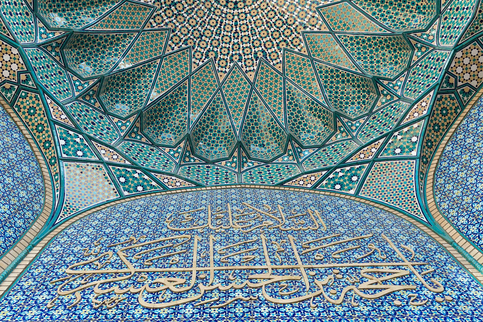 Calligraphy and turquoise geometric tilework beneath a mosque portal