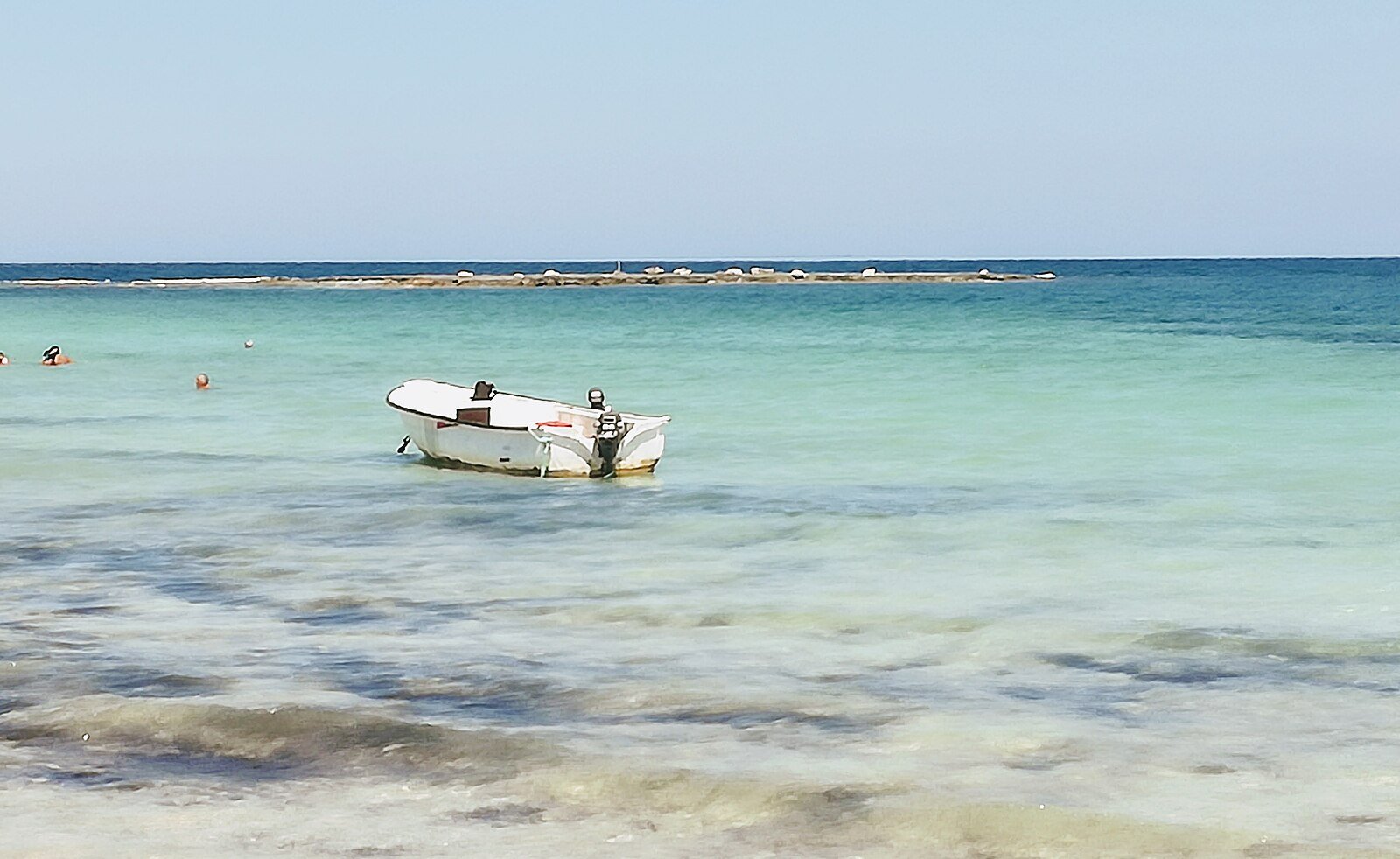 A small boat resting on clear turquoise shallows off a Djerba beach, Tunisia.