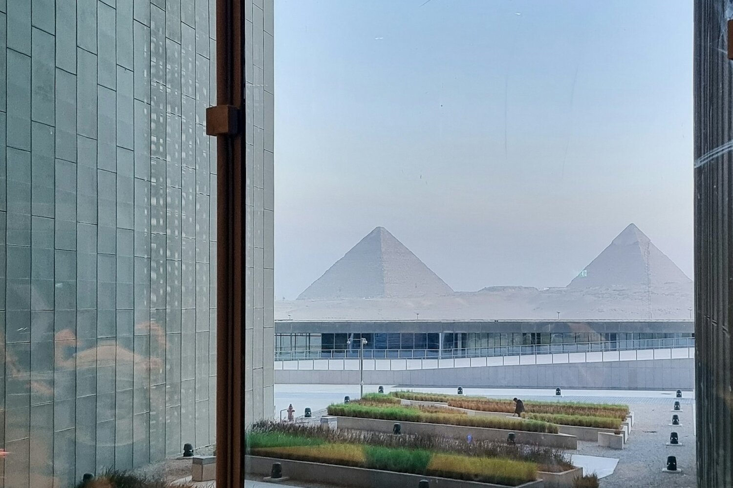 The Pyramids of Giza framed by the glass walls of the Grand Egyptian Museum