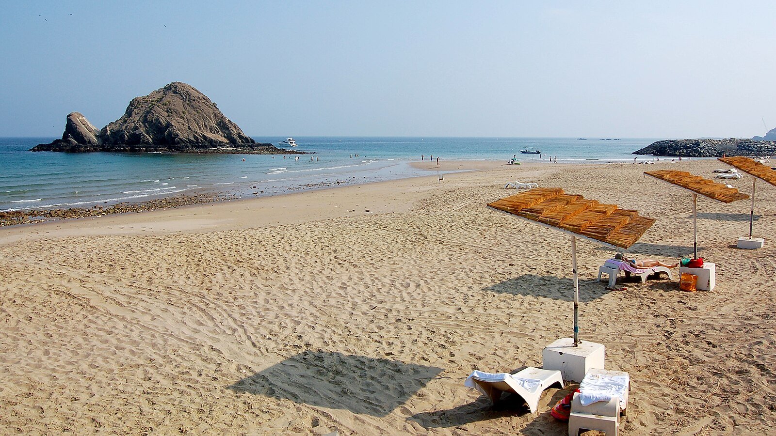 Shaded sun loungers on the golden sand of Al Aqah Beach, looking out to Snoopy Island in the Gulf of Oman