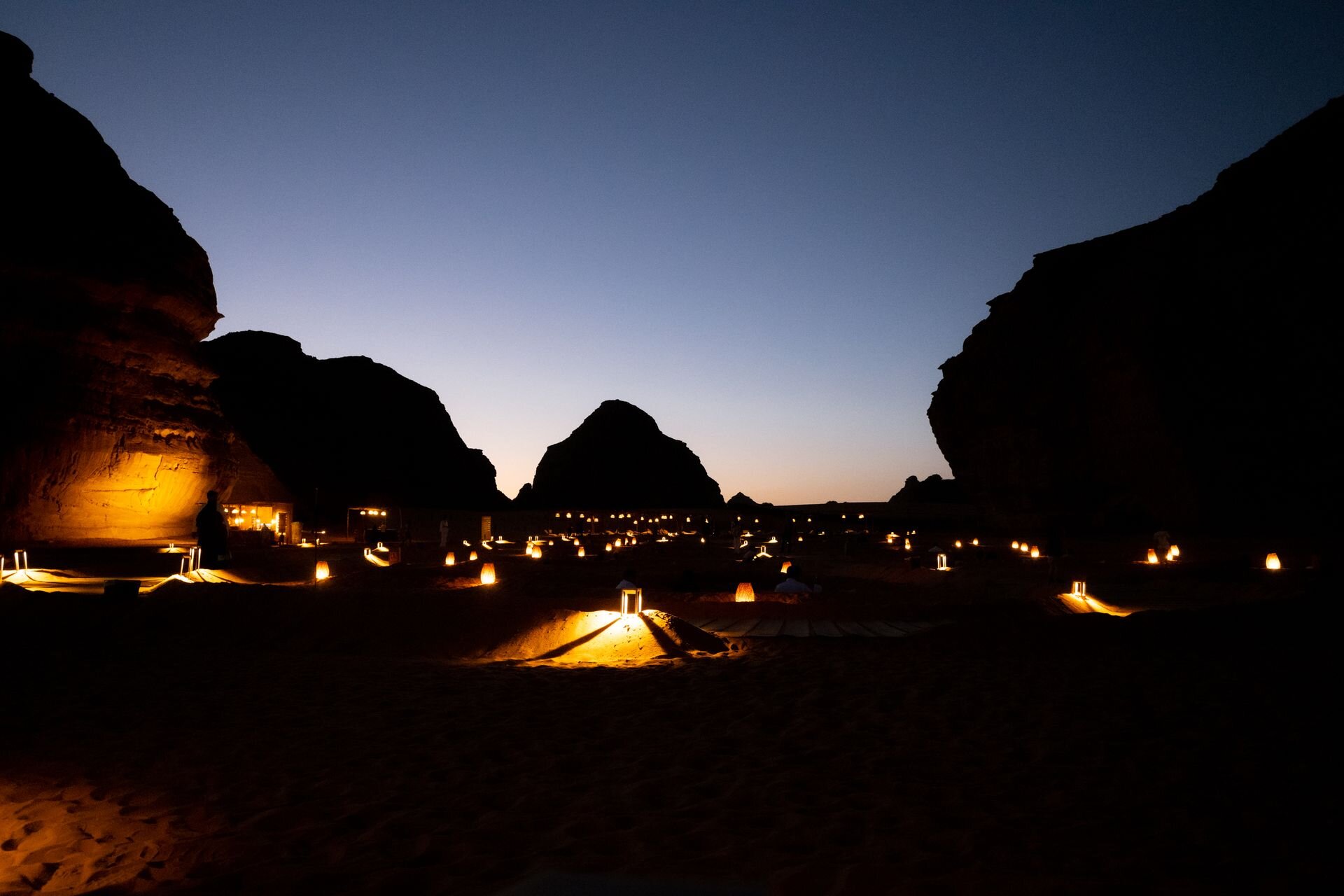 Lanterns glowing across a desert dinner among the sandstone rocks of AlUla at dusk