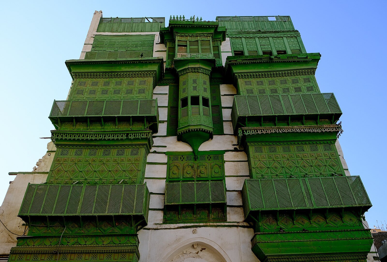 A traditional house in Al-Balad, Old Jeddah, its facade layered with green wooden roshan balconies.