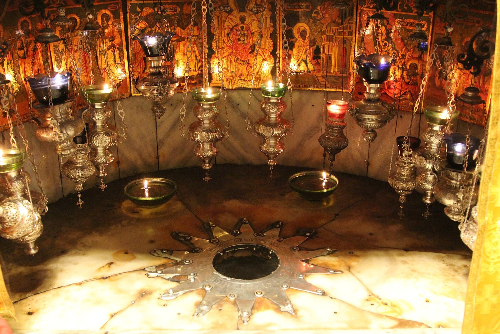 The silver star marking the traditional birthplace of Jesus in the Grotto of the Nativity, Bethlehem, beneath hanging oil lamps.