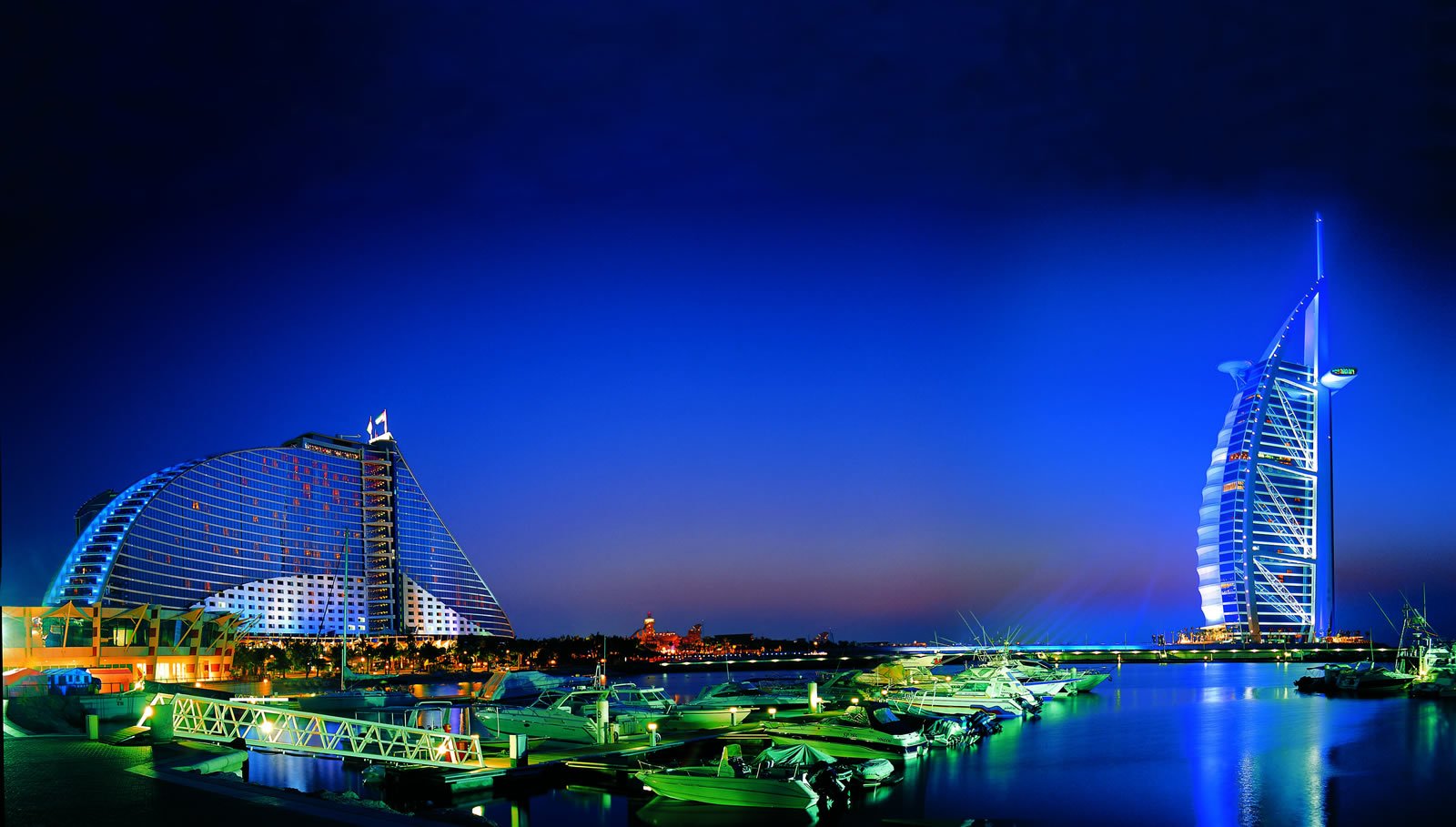 The Burj Al Arab and the wave-shaped Jumeirah Beach Hotel lit up at blue hour above the marina in Dubai.
