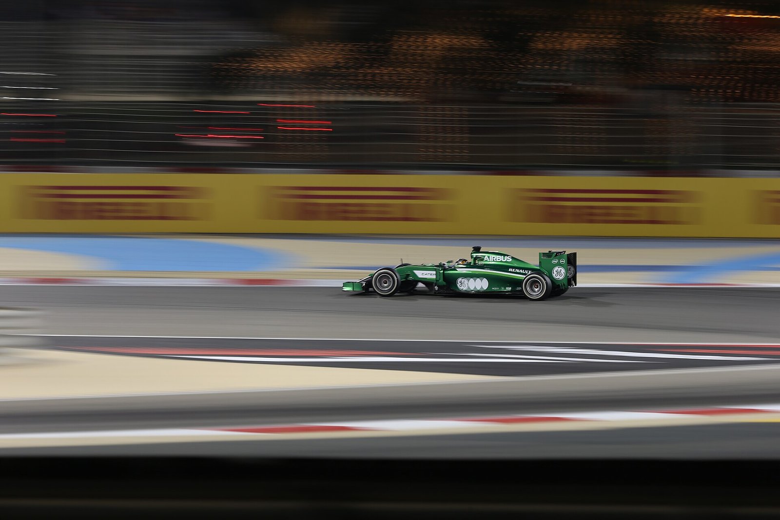 A Formula One car speeding past the trackside barriers under the floodlights of the Bahrain International Circuit.