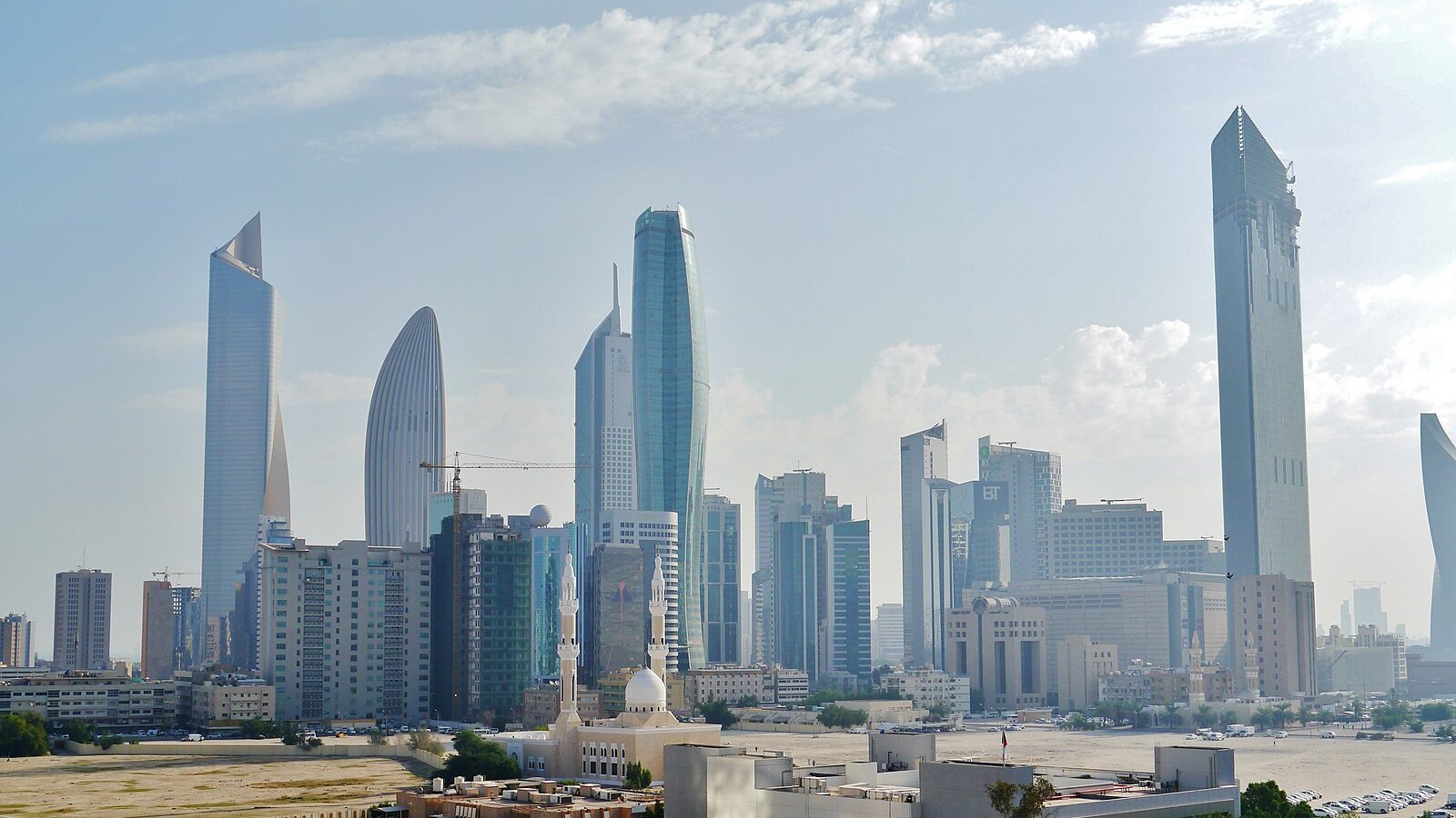 The glass towers of Kuwait City's central business district rising beneath a soft, cloud-streaked sky