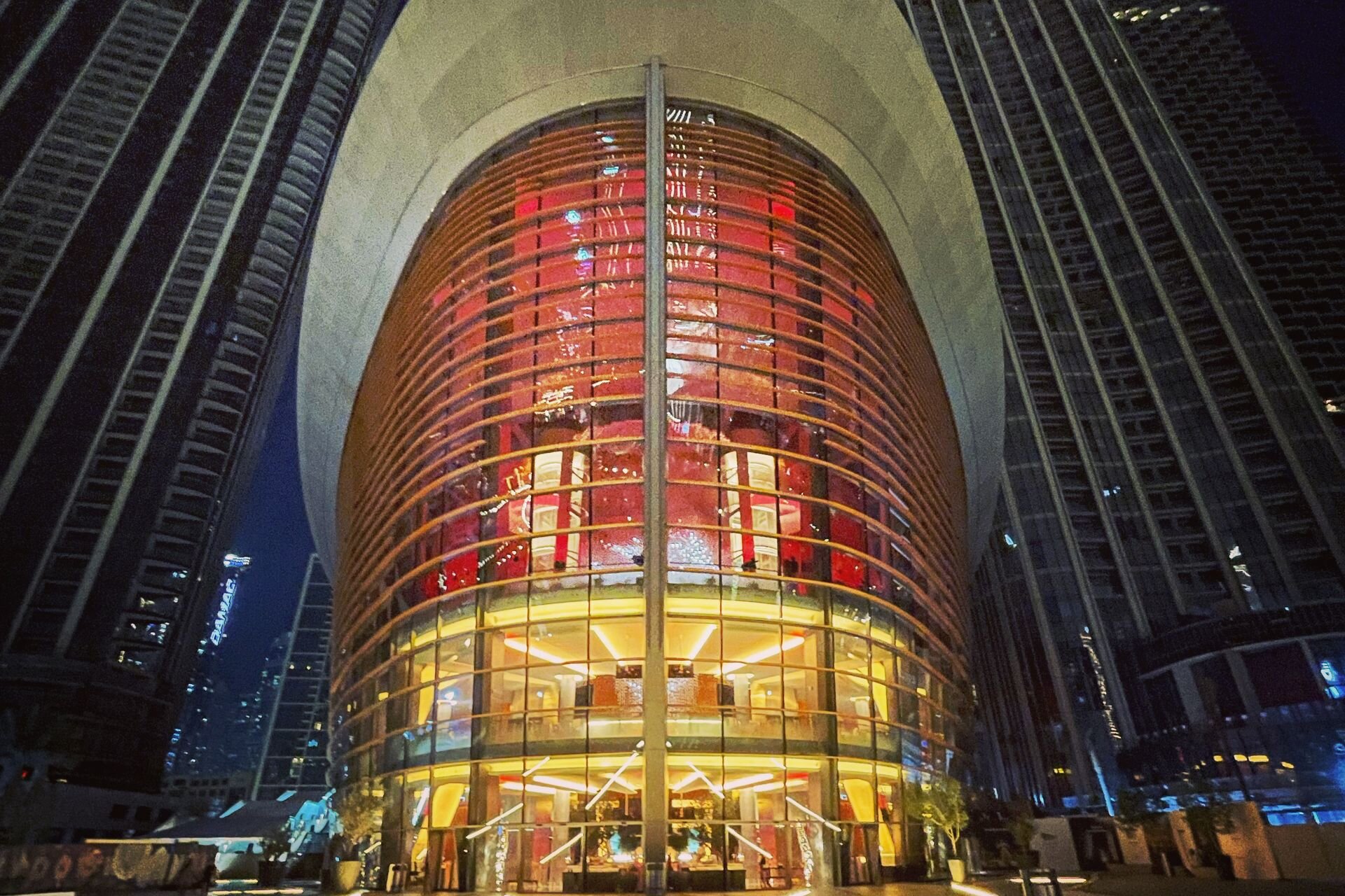 Dubai Opera glowing at night between the towers of Downtown Dubai