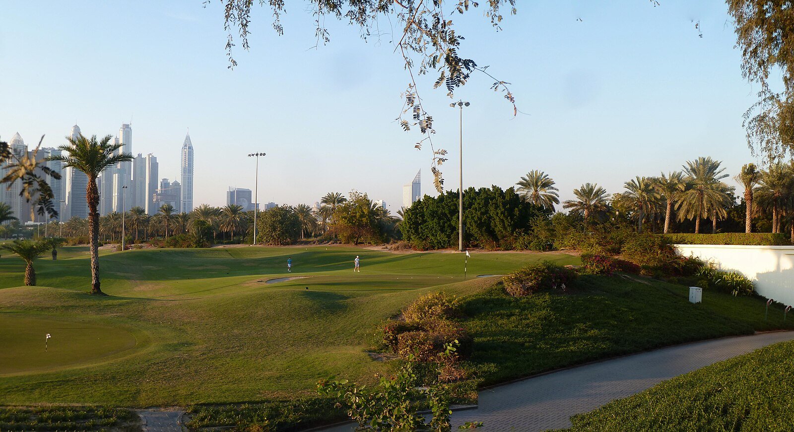 Palm-lined fairways of the Emirates Hills golf course in soft morning light, with the Dubai Marina towers beyond.