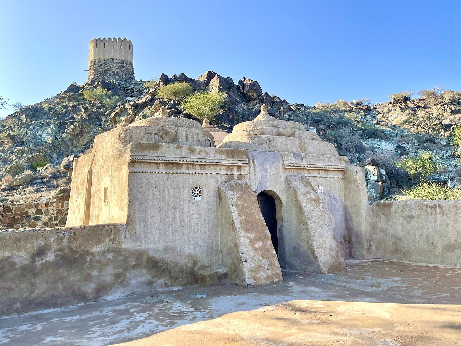 The domed clay walls of Al Bidya Mosque, the oldest known mosque in the UAE, below its hilltop watchtower