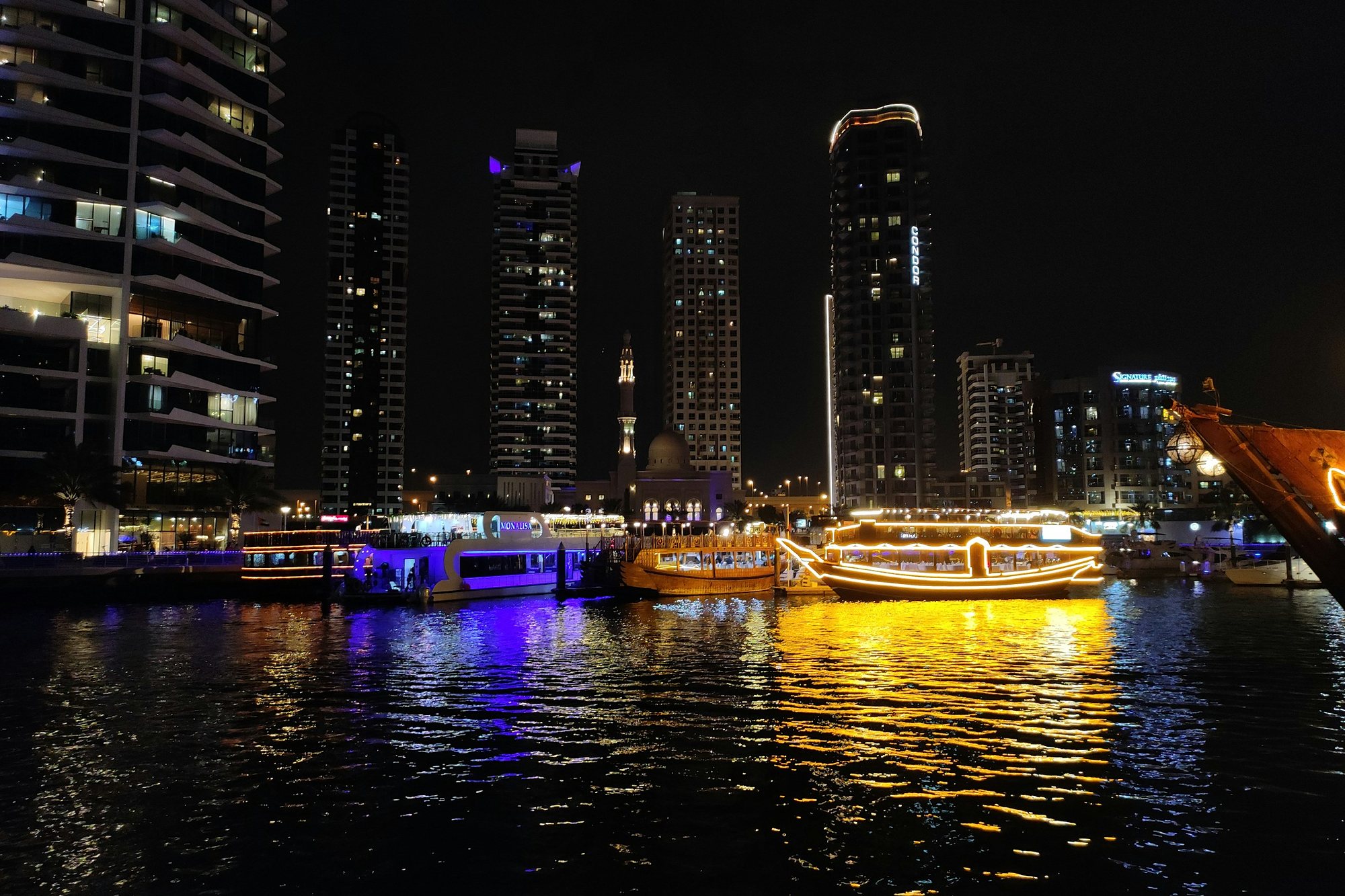 Lit dhows and a mosque minaret on the water at night in Dubai Marina