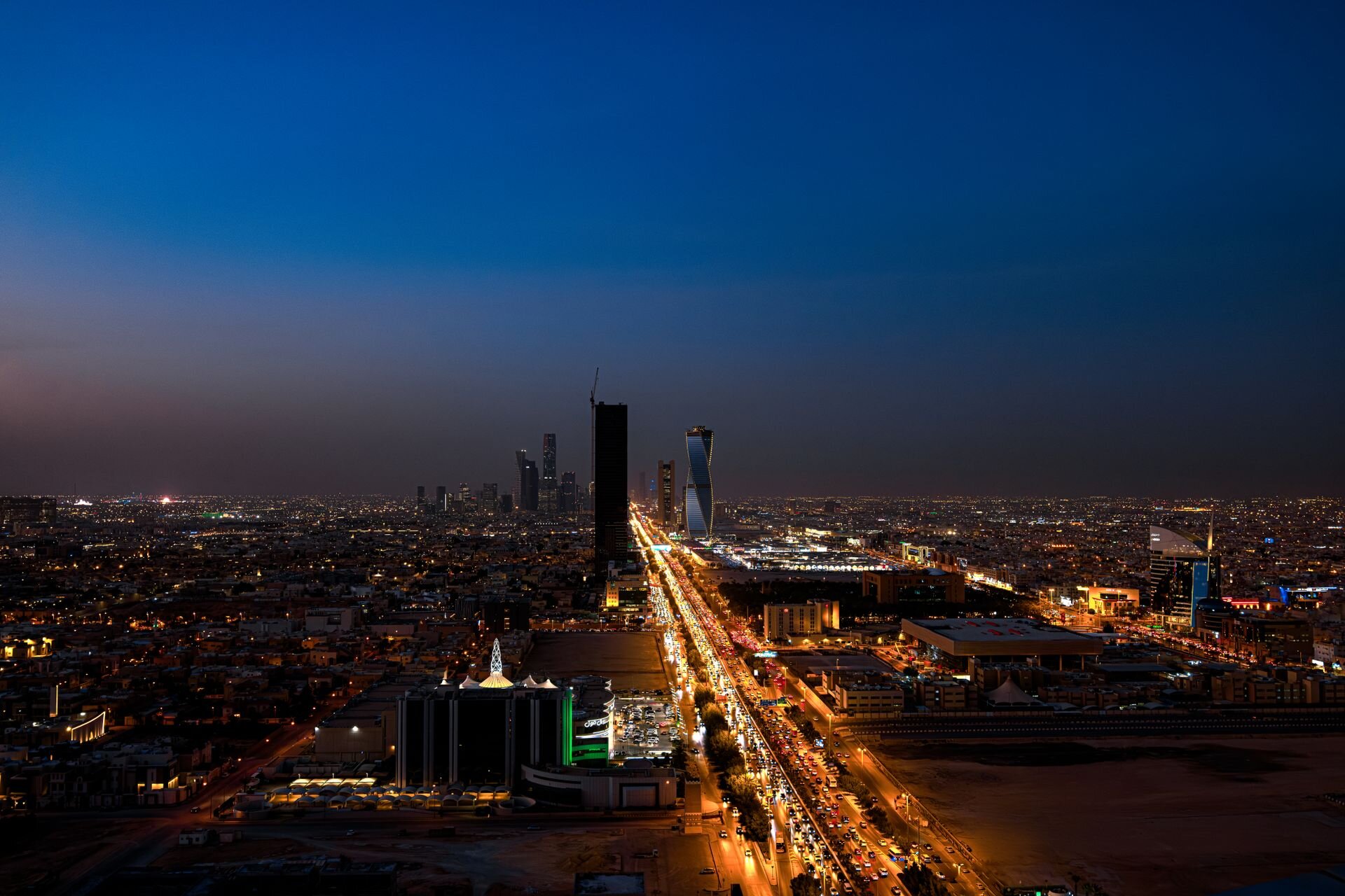 Riyadh at dusk from above, King Fahd Road running toward the new towers of the city
