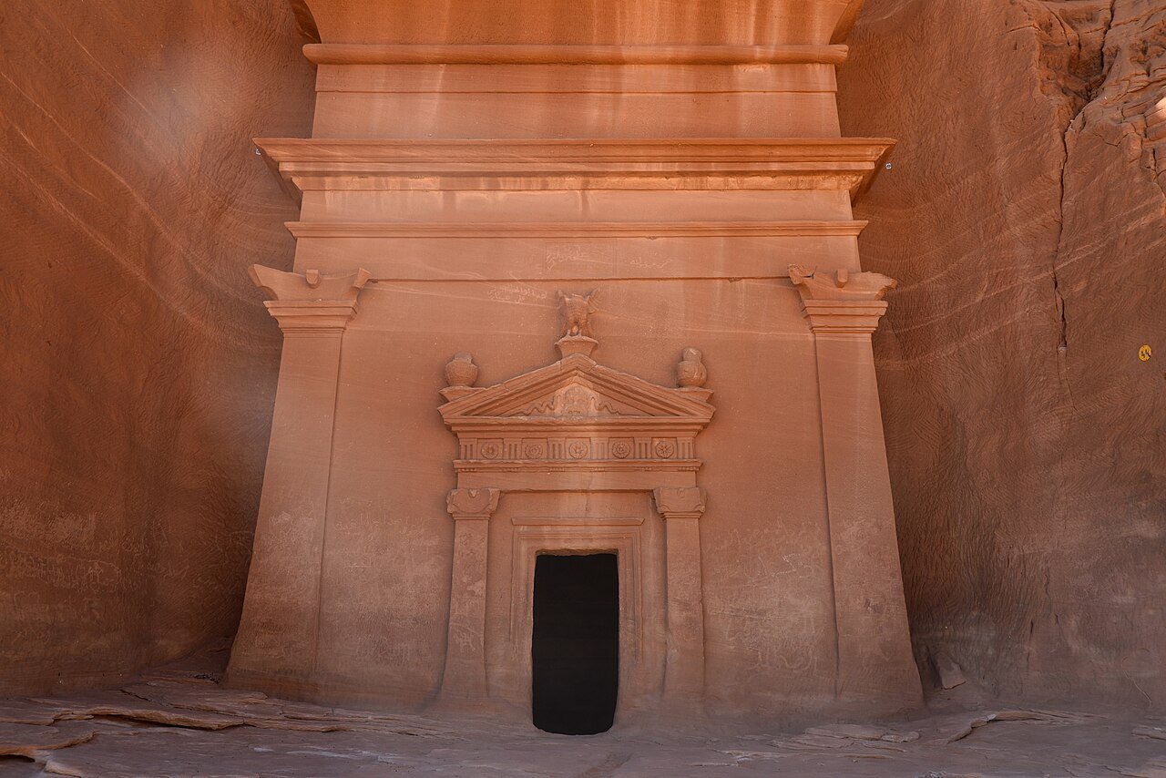 A carved Nabataean tomb facade cut into a rose sandstone outcrop at Hegra, AlUla.