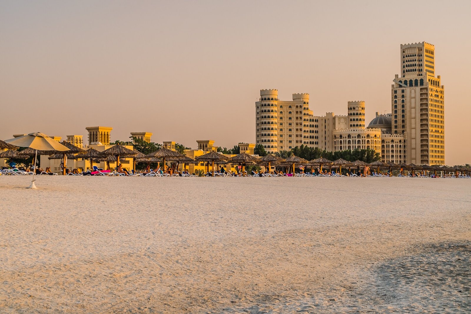 The beach at Al Hamra Village in Ras Al Khaimah at golden hour, with the Waldorf Astoria beyond the parasols