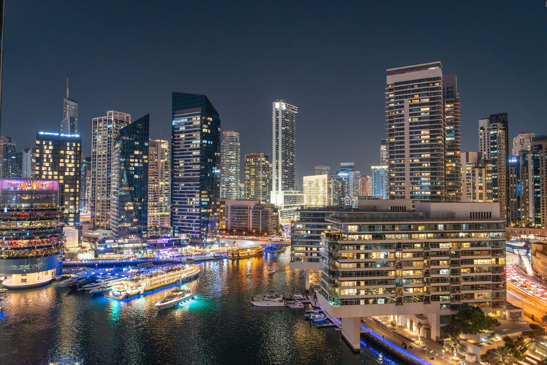 Dubai Marina lit up at night, yachts and dhows on the water below the towers