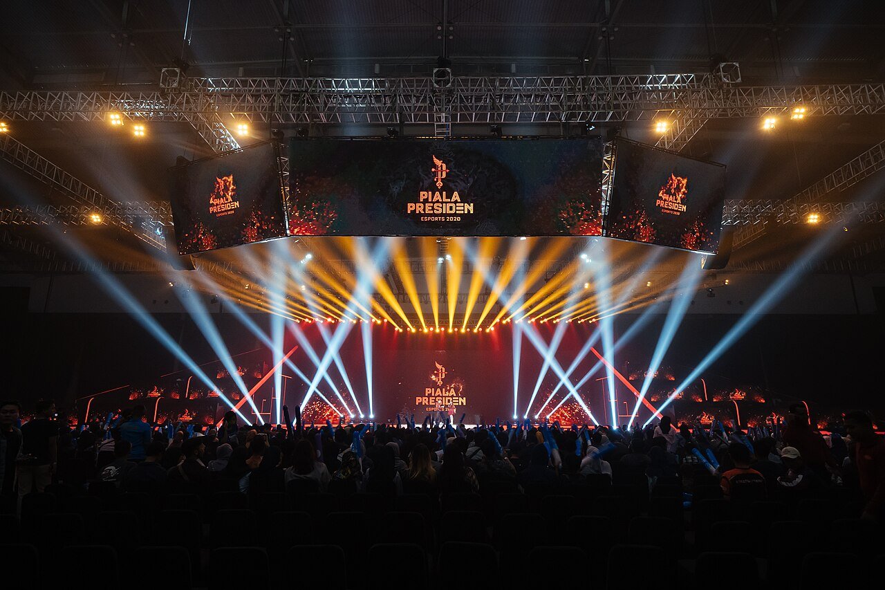 Beams of stage light sweeping over a packed esports arena during a national tournament final.